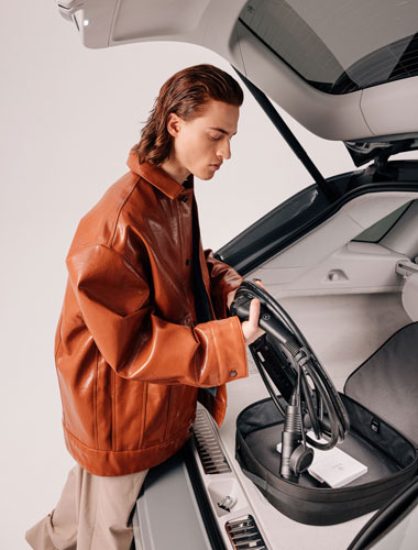 Abgebildet ist ein junger Mann in brauner Lederjacke, der ein Mercedes-Benz Ladegerät in den Kofferraum seines Autos legt.