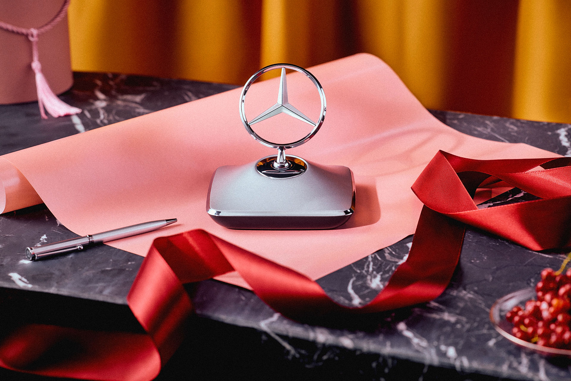 Gezeigt werden Mercedes-Benz Geschenkideen mit Briefbeschwerer in Sternform, Geschenkband und stilvoller Geschenkverpackung auf einem Marmortisch.