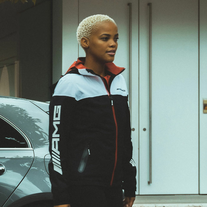 Frau lehnt an Auto und trägt AMG Jacke B66959290. Verlinkt auf Kategorie: Mode - Damen