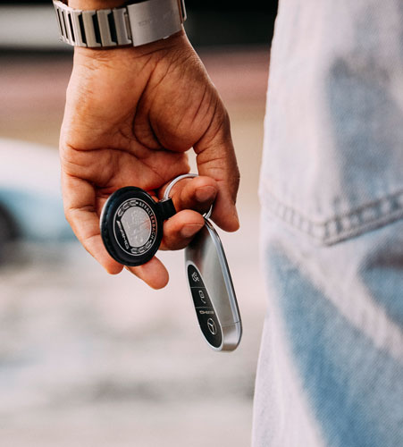 Mercedes-Benz Schlüsselanhänger Zu sehen ist ein Mercedes AMG Schlüsselanhänger, der an einem Autoschlüssel befestigt ist und von einer Person in der Hand gehalten wird.