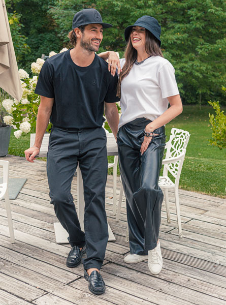 Mercedes-Benz Mode Kollektion Abgebildet sind ein Mann und eine Frau. Beide sind schwarz / weiß in der Mercedes-Benz Mode Kollektion gekleidet. Sie stehen auf einer Terasse vor grünem Hintergrund.